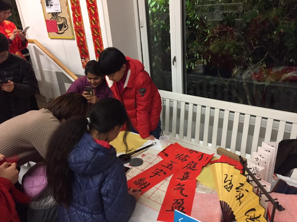 Several people are practicing Chinese calligraphy on a table with many different leafs of paper