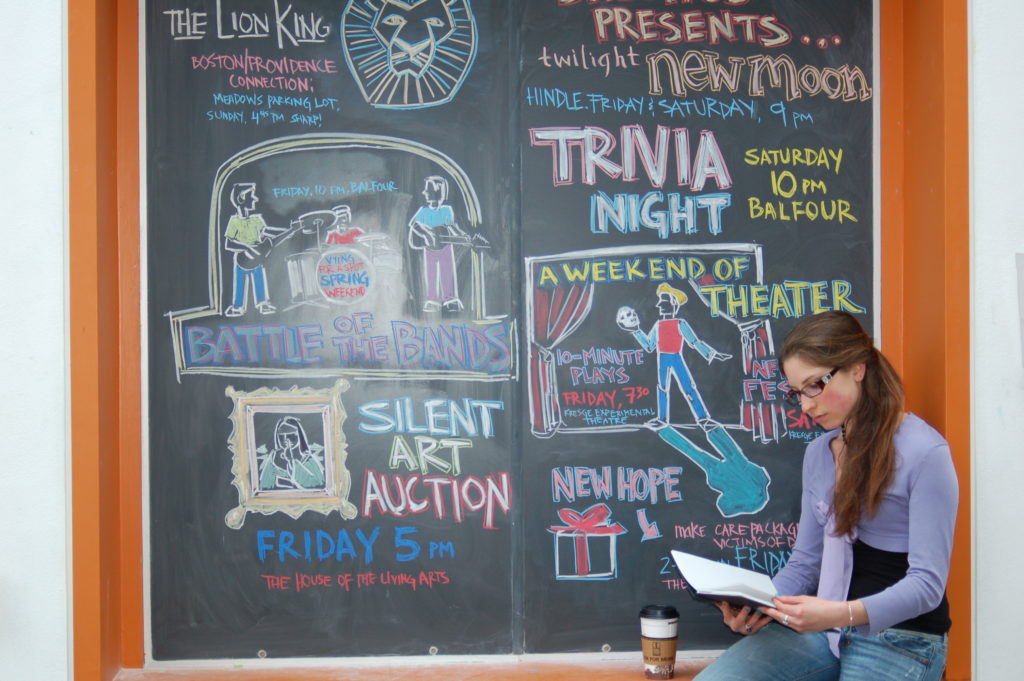 Student seated by chalkboard listing campus events