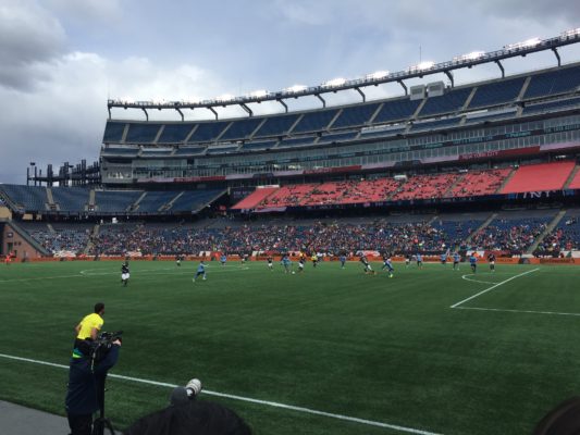 There is agreen field with players running around playing soccer