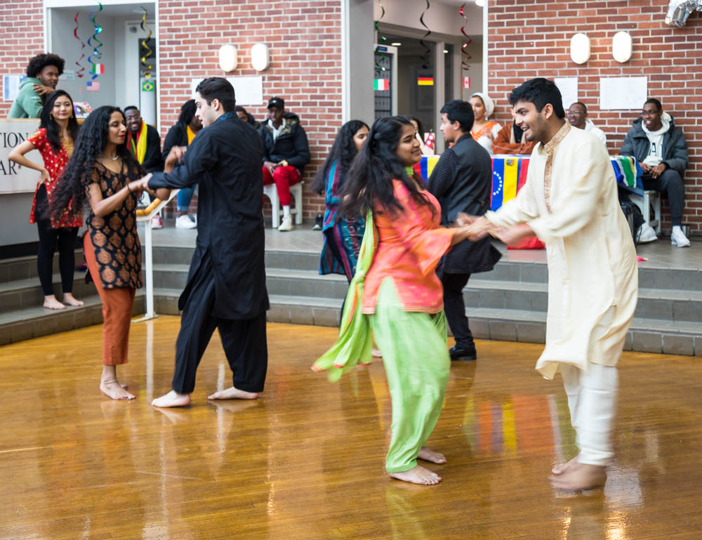 Photo of students in traditional clothing doing a Bollywood dance on a wooden floor with spectators watching