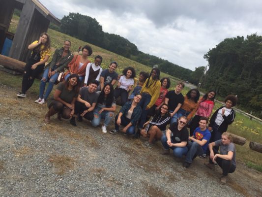 This is a group photo of students standing in front of a fence by a pumpkin patch