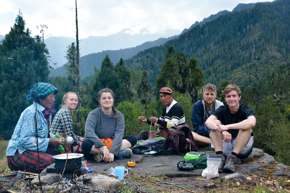 A group photo of students sitting in front of a campfire drinking tea in the mountains of Bhutan