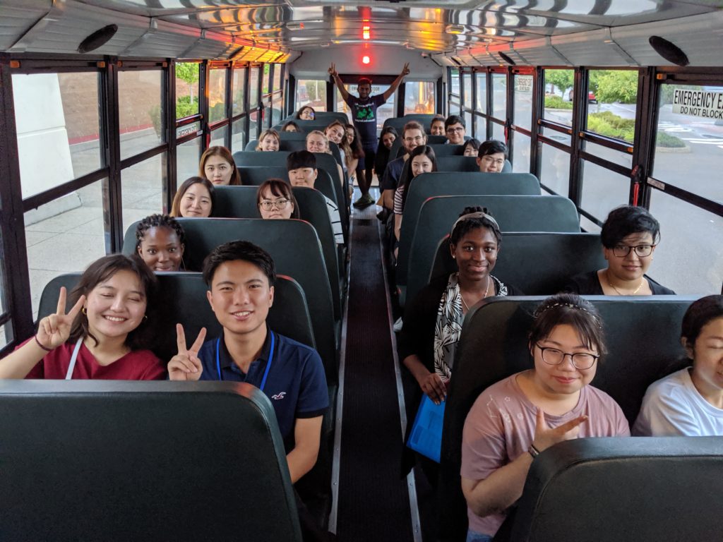 A group of students on a bus smiling and waving at the camera