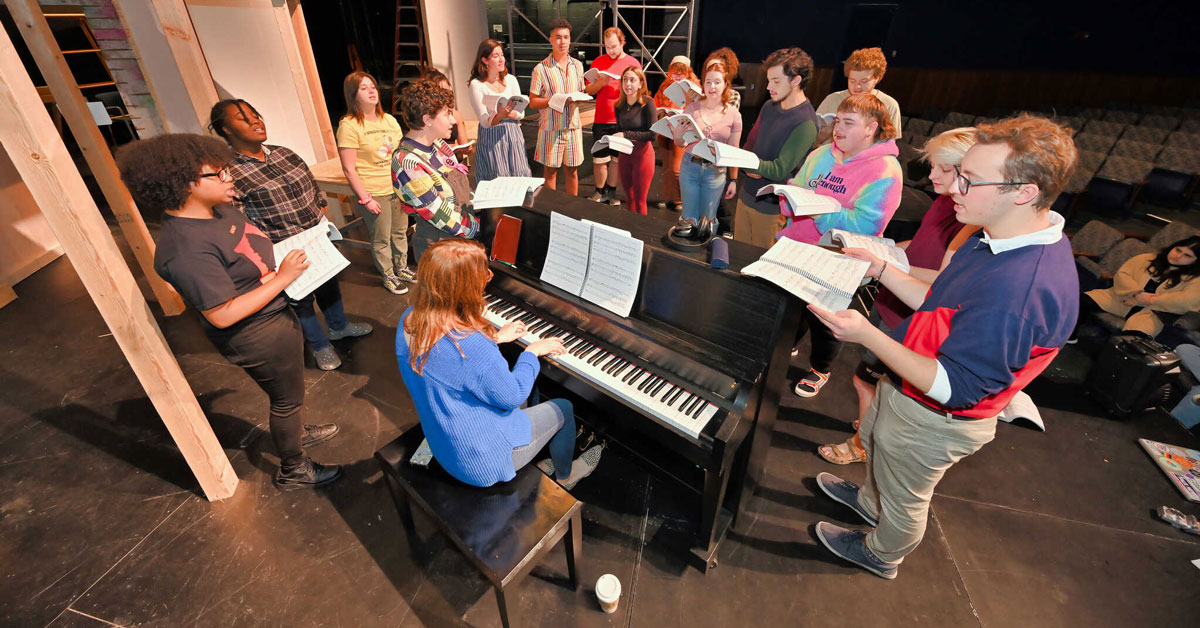 "Rent" cast and crew gathered around piano rehearsing