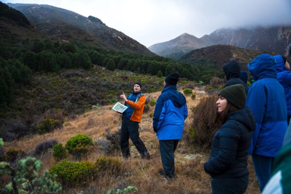 A professor talking to a group of students, standing in front of mountains.