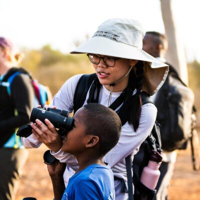 A student holding binoculars for a child to look through.