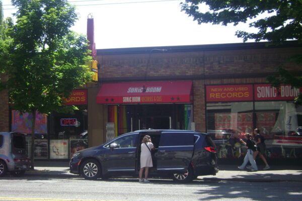 A car with a person standing in front of it, in front of a record store.