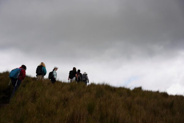 A group of people walking on a ridge together with a cloudy sky behind them.