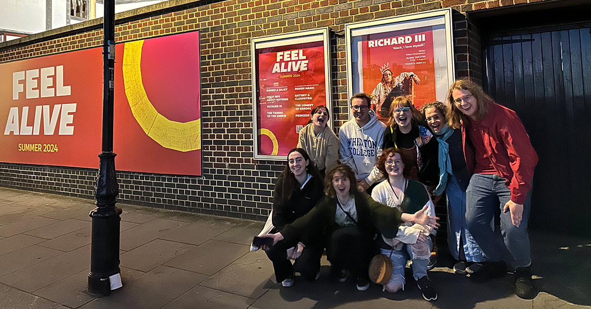 A group of eight smiling individuals gather outside the Globe Theatre in London.