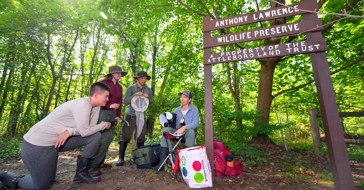 Four individuals wearing long-sleeved shirts, pants and hats talk outside a sign reading Anthony Lawrence Wildlife Preserve