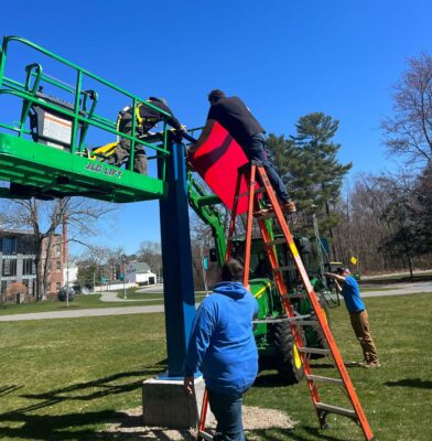 Several lifts are used for individuals to complete assembly of a metal sculpture.