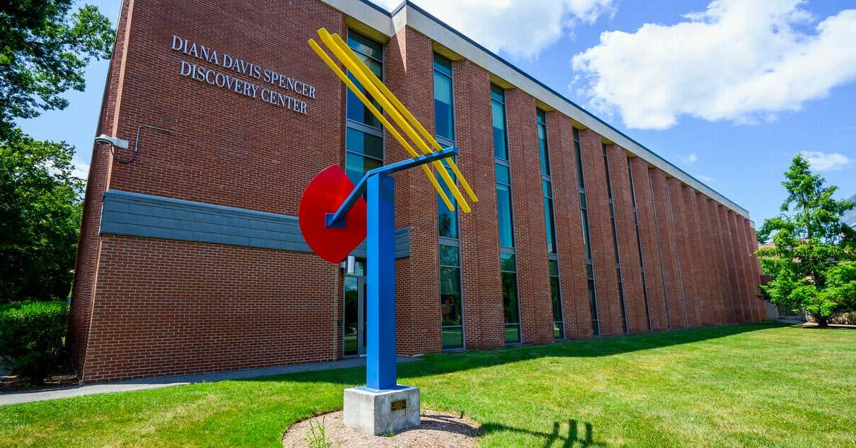 A blue, red, and yellow sculpture was installed outside a brick building.