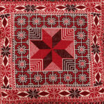 Detail of pillow with tatreez pattern of the star of Bethlehem in shades of red on cream
