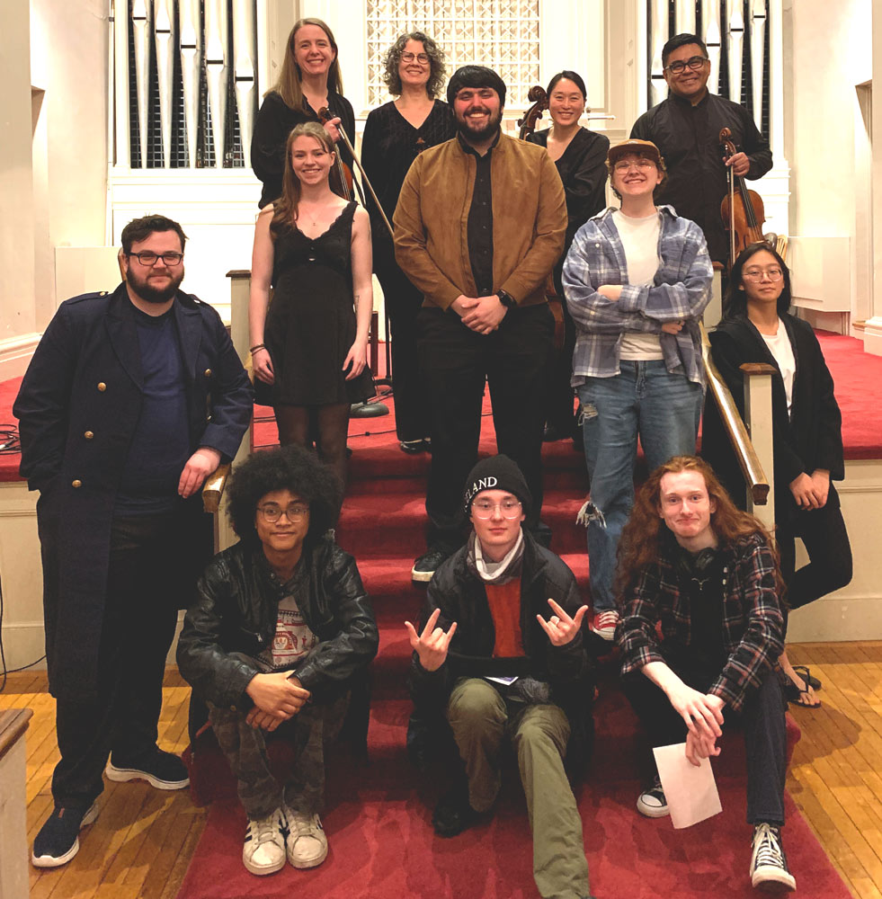 A group of 12 individuals gathered in front of a pipe organ.