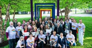 Graduates, staff, and faculty are seen around the Rainbow Arches on campus, all wearing Wheaton Pride shirts. 