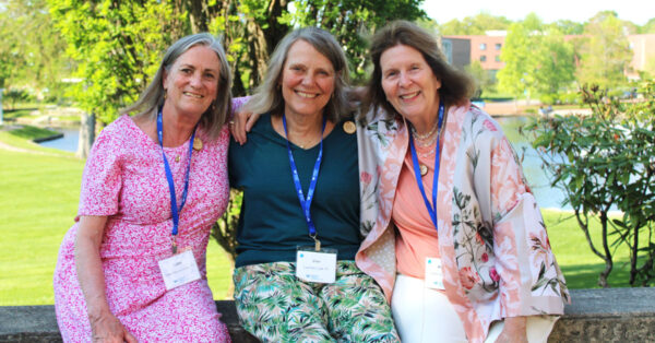 Three smiling women sitting with their arms around each other's back.