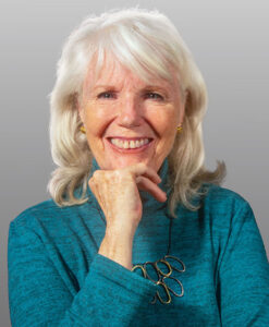 A smiling woman with white hair wearing a turquoise shirt.