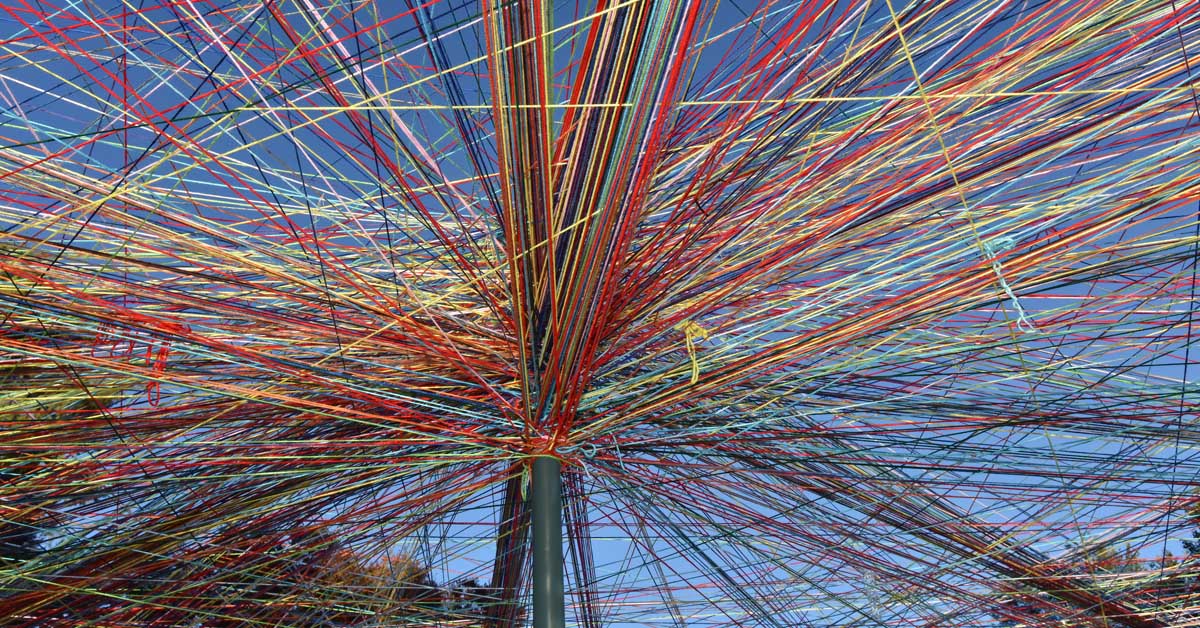 Hundreds of skeins of different colors of yarn are tied to a pole and tied to other poles on its perimeter, creating a web-like public art display.