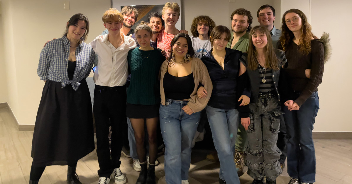 A group of 13 smiling college students, dressed in casual attire.