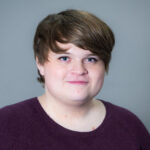 An individual with brown hair wearing a plum colored shirt