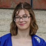A smiling woman with brown hair wearing glasses and a blue shirt