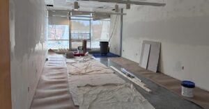 Classroom without furniture, protective floor coverings, and construction material lined up against the far window.
