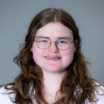 A smiling woman with long brown hair wearing glasses and a white shirt