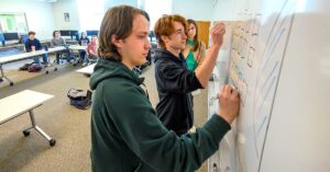 Two students are actively engaged in writing on a whiteboard.