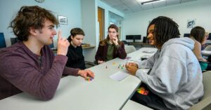 Four young adults engaged in a discussion around a table in a classroom setting.