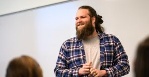 Professor talks to a classroom of students, several of whom appear in the foreground of the image.
