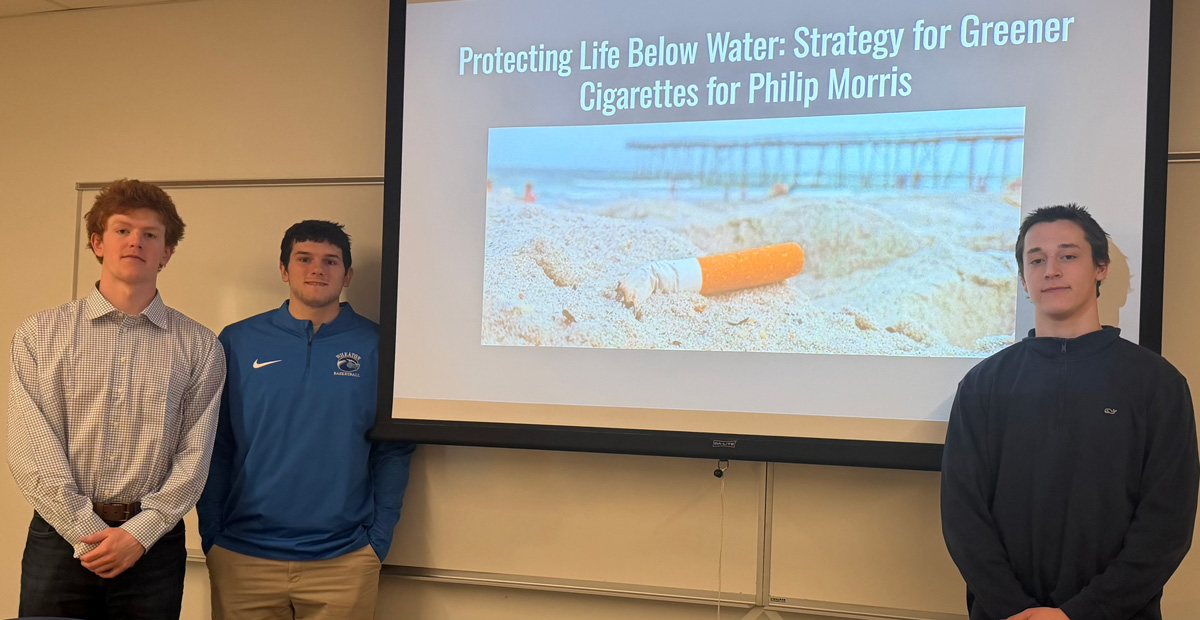 Three young men stand beside a projected screen with an image of a cigarette butt in the sand on a beach. The text reads Protecting life below water: strategy for greener cigarettes for Philip Morris