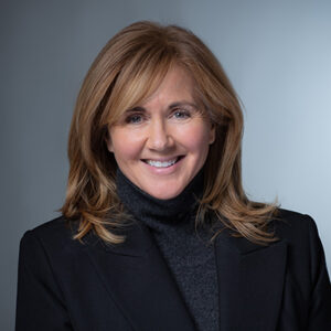 A smiling woman with brown hair wearing a dark sport coat.