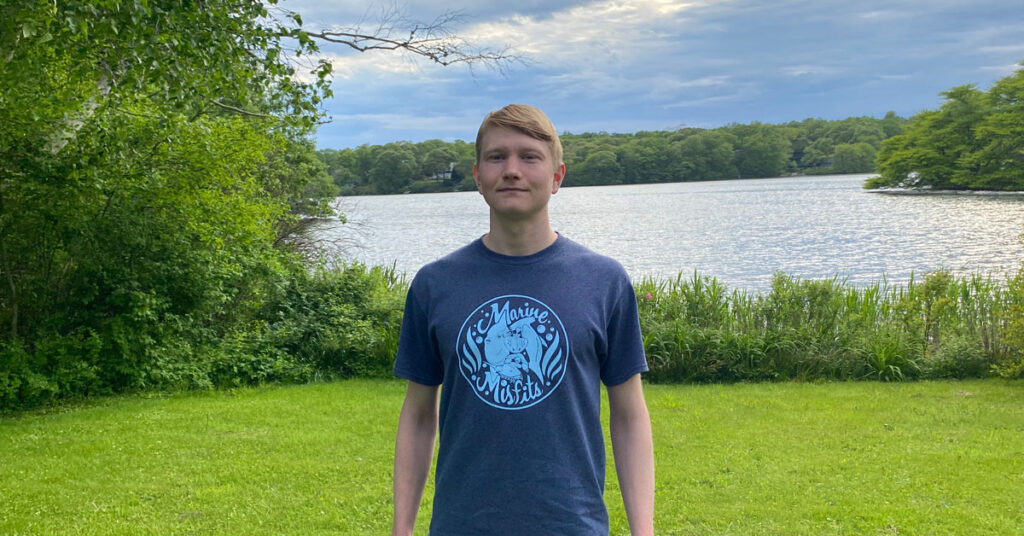 Student stands in a clearing near an inlet bordered by salt marsh grass.