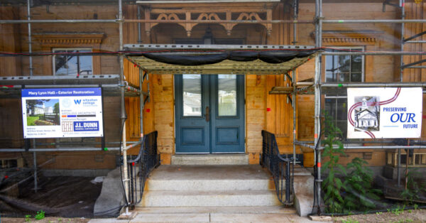 Scaffolding surrounds the paint-stripped wooden exterior and main entrance of Mary Lyon Hall during restoration at Wheaton College.