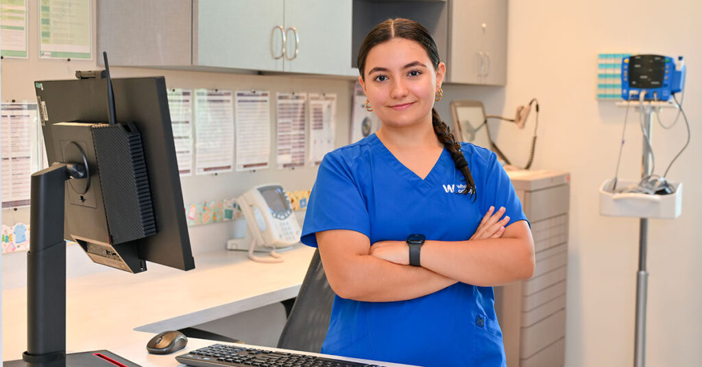 Wheaton College nursing student Ashley Almeida wears blue scrubs in a clinical setting.