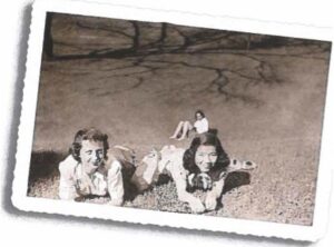 Black-and-white vintage photograph of Momo Nagano and a classmate lying on the grass together outdoors on a sunny day.
