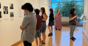 A group of college students in an art gallery viewing wall-mounted black-and-white historical photographs and archival documents during an exhibition.